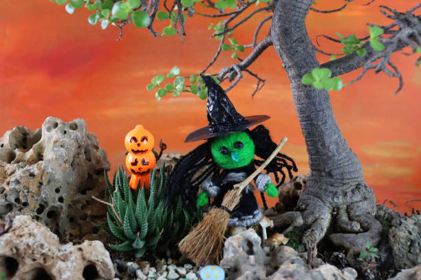 istock Image of autumnal Halloween scene, model string witch and broomstick standing on green grass with autumnal leaf hedge and orange sunset sky 1264332452