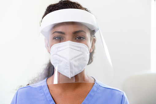 A female doctor arrives for her shift on the COVID-19 ward in a hospital. She is wearing a protective face shield over a N95 face mask.