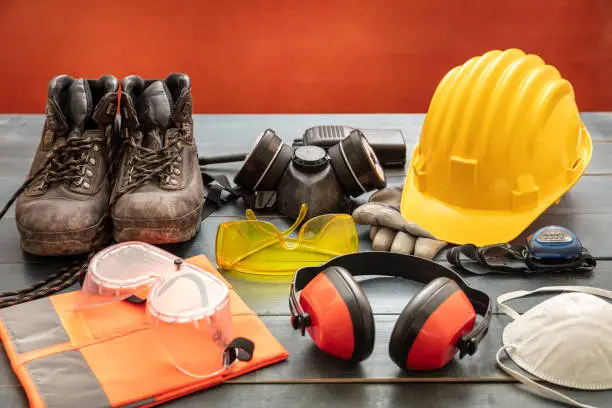 Photo of Work safety protection equipment. Industrial protective gear on wooden table, red color background.