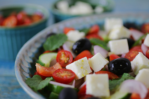 Stock photo showing a close-up view of healthy eating image of a salad bowl containing a horiatiki (Greek) salad with tomatoes, cucumbers, onion, feta cheese, mint leaves and black olives.