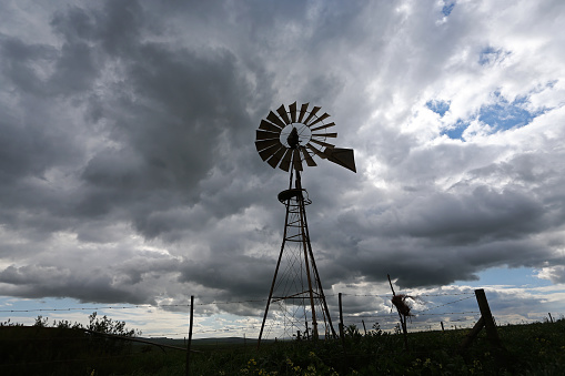 A silhouette of a water pump windmill against a cloudy sky on a farm in Cape Town, South Africa