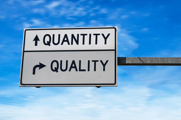 istock Quantity versus quality. White two street signs with arrow on metal pole. Directional road. Crossroads Road Sign, Two Arrow. Blue sky background. 1264336013