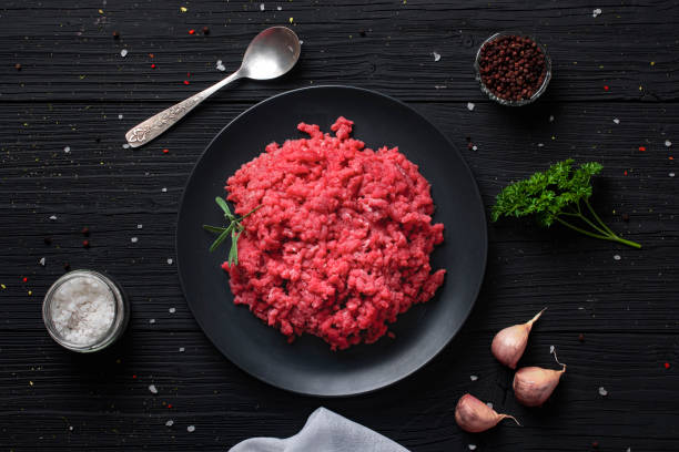 istock Black plate with minced meat on a black wooden table. View from above. 1264337147