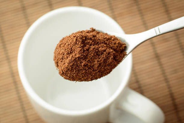 istock Spoon with ground coffee over the white empty cup against a brown bamboo background 1264338065