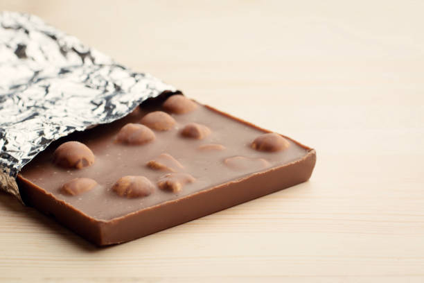 Bar of chocolate covered with foil lays on light wooden background.