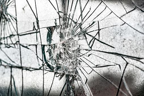 A close-up of a shattered windshield, showing the impact point and the cracks radiating outwards the car hit a butternut dropping out of a tree at 45 MPH
