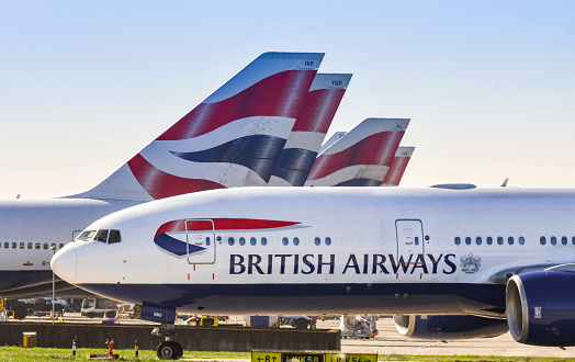 London, England - March 2019: Boeing 777 long haul airliner operated by British Airways taxiing for take off past tail fins of the company's other aircraft.