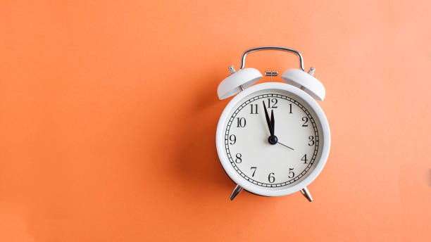 banner white alarm clock on a colored orange background. minimalism. art concept of time, start, planning. copy space. - clock time alarm clock orange imagens e fotografias de stock