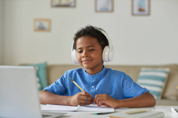 istock Content curious African-American boy in wireless headphones using laptop while talking to tutor via video conferencing app 1264348866