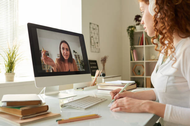 istock Online tutor assisting student girl with coursework during video conference, student girl with curly hair making notes 1264349083