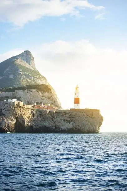 Photo of Trinity lighthouse at the rocky shore (cliffs) of the Europa Point. British Overseas Territory of Gibraltar, Mediterranean sea. Epic cloudscape. National landmark, sightseeing, travel destination