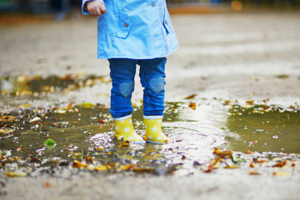 istock Child wearing yellow rain boots and jumping in puddle on a fall day 1264350473