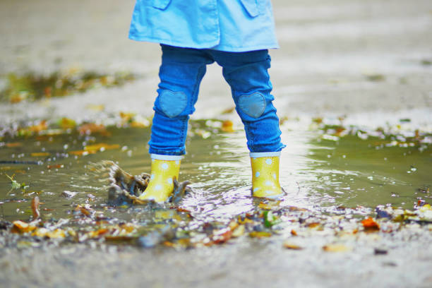 istock Child wearing yellow rain boots and jumping in puddle on a fall day 1264350482