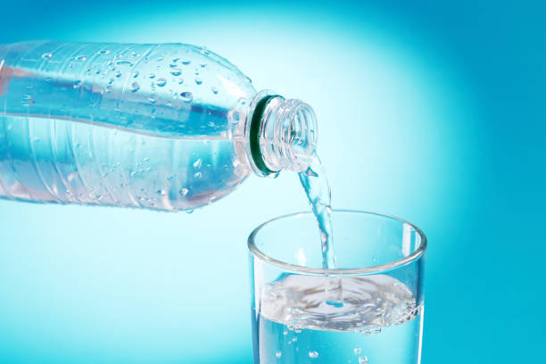 青い背景の上にガラスに新鮮なボトル入り飲料水を注ぎます。コピースペース。水の流れ。エネルギーシンボル概念 - overflowing water glass bottle ストックフォトと画像