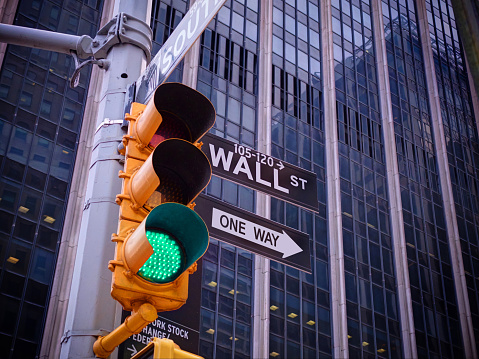 View on wall street yellow traffic light with black and white one way pointer guide. Green traffic light to Wall street banks money dollars finance offices. New York traffic light on Wall street money