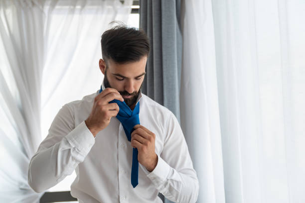 Young businessman man with beard tie his neck tie preparing for new job interview in new company or he is a groom preparing for the wedding Young businessman man with beard tie his neck tie preparing for new job interview in new company or he is a groom preparing for the wedding necktie fashion adjusting suit stock pictures, royalty-free photos & images