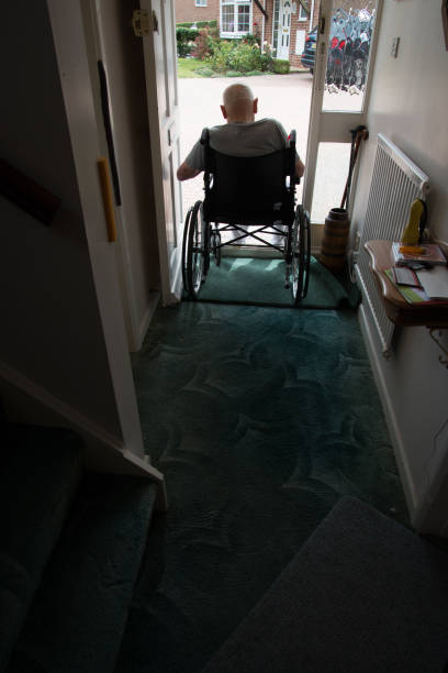 старик в инвалидной коляске смотрит из открытого дверного проема своего дома. хэмпшир, великобритания. - housebound стоковые фото и изображения
