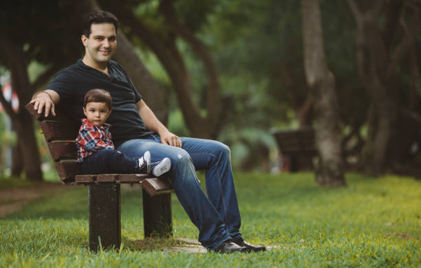 istock Baby boy sitting with father on a park bench. 1264354152