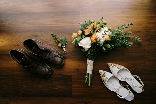 The bride's bouquet with large white roses and the groom's boutonniere with women's white shoes and men's brown shoes with untied laces. High quality photo