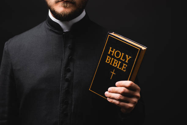 istock cropped view of priest holding holy bible isolated on black 1264355267