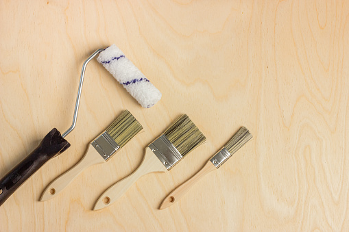 New paint brushes and paint roller on wooden background. Home renovation or DIY concept, flat lay. Copy space.