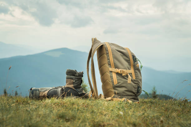 istock Khaki color boots and backpack standing on a grass on top of a mountain hill. 1264356218