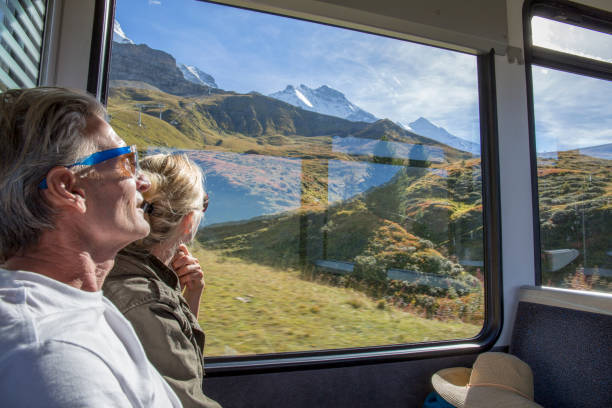 Mature couple in moving train enjoy the passing views Sunny Swiss alps and alpine area outside train interior stock pictures, royalty-free photos & images