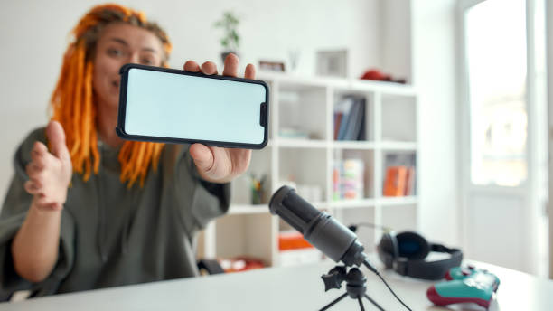istock Results. Female technology blogger with dreadlocks showing smartphone with blank screen while recording video blog or vlog in the daytime 1264357118