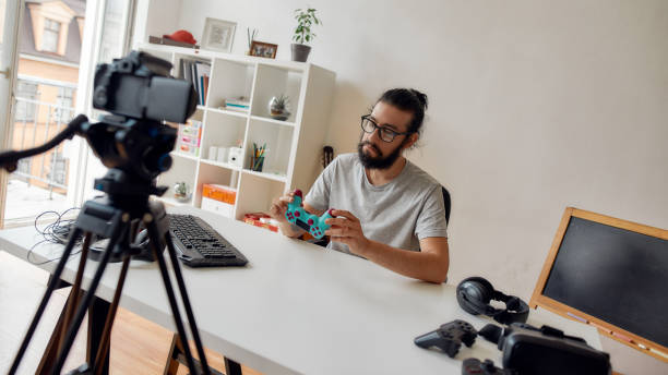 istock Male technology blogger in glasses looking at game controller joystick, holding it while recording video blog or vlog about new gadgets at home 1264358079
