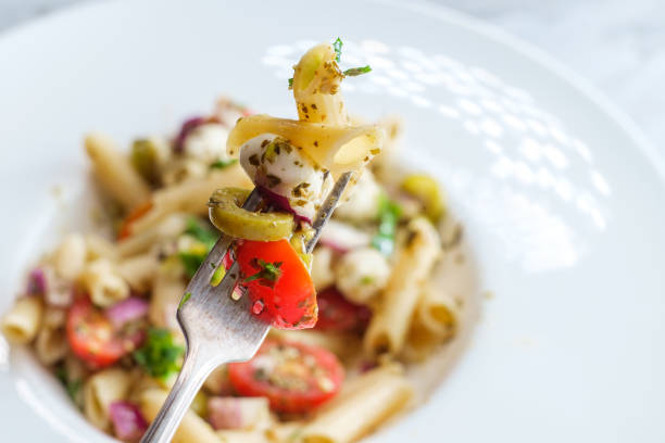 Gluten free Italian pesto pasta salad with pearl mozzarella cheese balls and halved cherry tomatoes