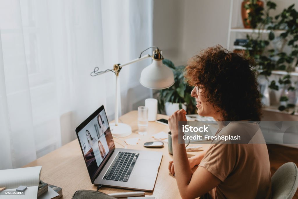 Happy Woman Talking to Friends in a Video Call, Coronavirus Prevention Concept Smiling woman in a group video chat with friends/colleagues on her laptop pc. Adaptation - Concept Stock Photo