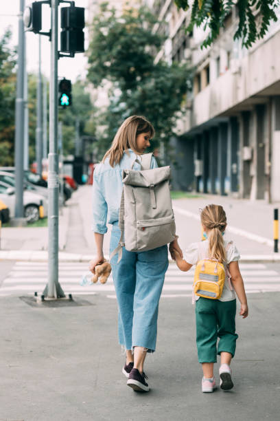 primo giorno di scuola: un simpatico bambino di prima elementare che va a scuola con sua madre - rear view family isolated child foto e immagini stock