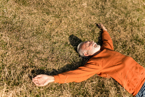 Joyful senior man laying on the ground and meditating.