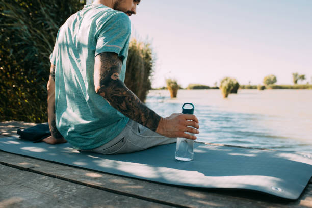 Man Sitting on a River Bank and Doing Yoga