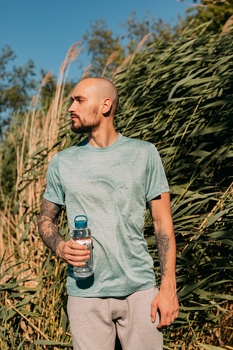 Hydration is important: a handsome sportsman holding a water bottle while working out outdoors.