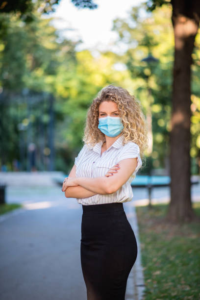 istock Businesswoma walking through park with her protective mask on her face 1264372515