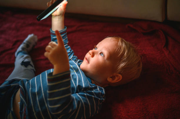 Cute boy holding mobile phone and lying on back on the floor