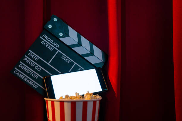 istock mobile phone with empty white bright screen with popcorn bucket and movie clapper board. Concept of streaming TV on internet phone. 1264380423