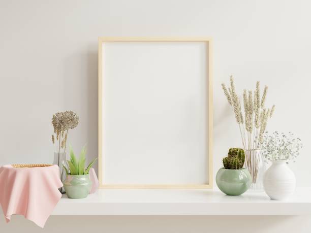 istock Wooden frame leaning on white shelf in bright interior with plants on the table with plants in pots on empty wall background. 1264383883