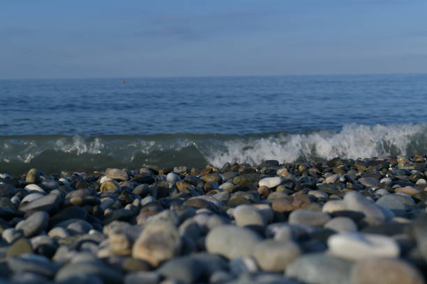 Seascape overlooking the blue sea and foamy swirling wave with a splash from the side of the pebble shore, in the dawn rays.