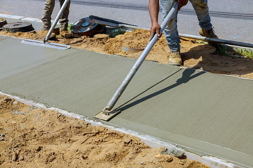 Worker plastering the concrete cement during construction contractor using a float to sidewalk
