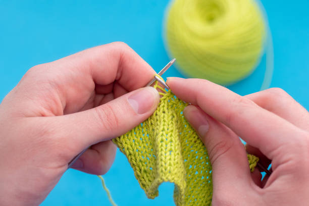 istock Close-up female hands knit on a knitting needle classic pattern of green threads on a blue background, copy space 1264406550