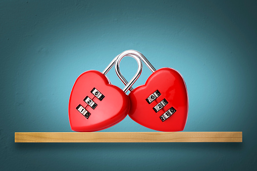 Single red padlock with heart on it connected to a chain, brown blurred background, horizontal