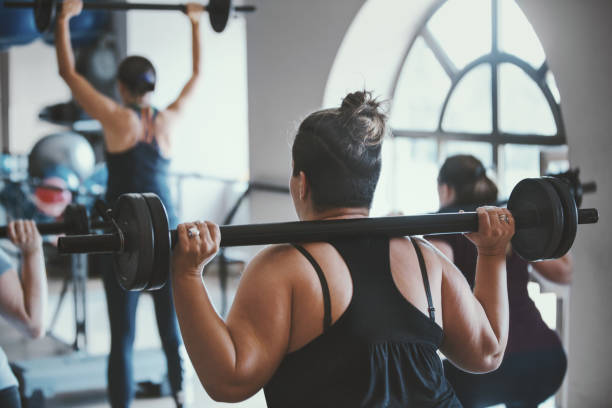 mulher acima do peso fazendo agachamentos de peso na academia. - crouching exercising women barbell - fotografias e filmes do acervo