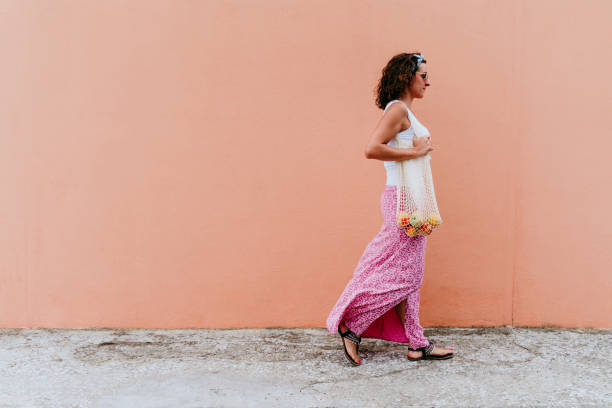 mulher andando pela cidade, segurando um saco de algodão com frutas. conceito de lixo ecológico e zero - earth cheerful orange white - fotografias e filmes do acervo