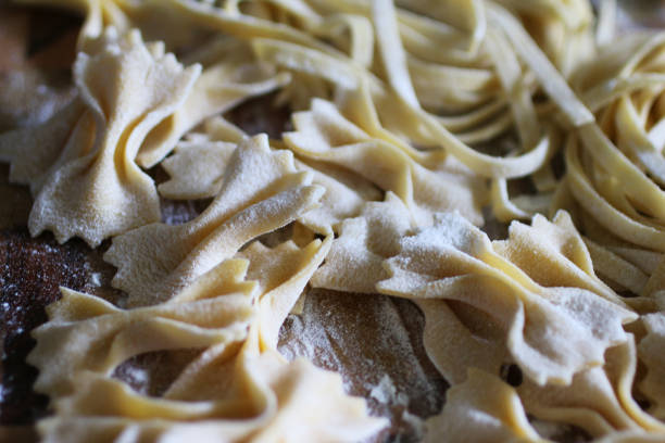 bild von hausgemachten tagliatelle nester und farfalle pasta (bowtie oder schmetterling) teig in mehl abgestaubt und auf bemehlten holz schneidebrett trocknen gelassen, erhöhte ansicht der italienischen küche - pasta raw traditional culture heap stock-fotos und bilder