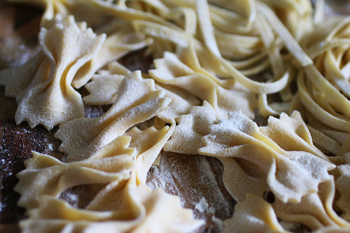 Stock photo showing elevated view of Italian cuisine. Home made Farfalle and tagliatelle pasta left to dry on floured wooden chopping board.