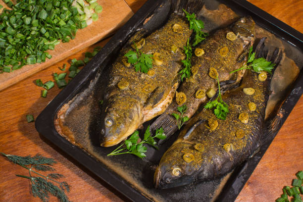 The tench fish is baked in the oven The tench fish is baked in the oven and seasoned with spices, fried onions and fresh green parsley leaves.Next to the fish is chopped green onions and dill leaves. tinca tinca stock pictures, royalty-free photos & images