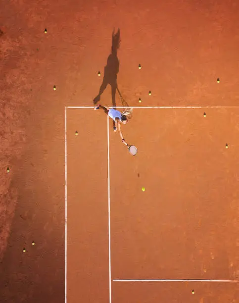 Photo of Healthy lifectyle. A young girl plays tennis on the court. The view from the air on the tennis player. Dirt court. Sport background. Aerial view from drone.