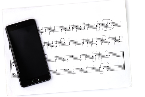 Cell phone with black blank screen and music sheet isolated on white background